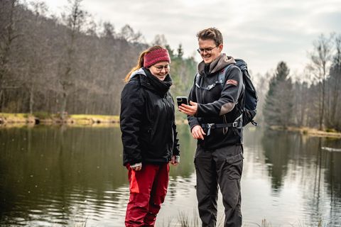 Zwei Personen stehen am Fischweiher in Friedrichstal und schauen auf ein Handy.