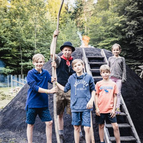 Vier Kinder stehen mit Thomas Faisst vor seinem Kohlenmeiler in Baiersbronn.