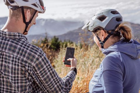 Zwei Biker stehen auf einem Berg und schauen auf ein Smartphone.